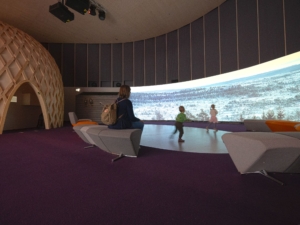 Ihmisiä näyttelytilassa jossa iso luontomaisema taustalla