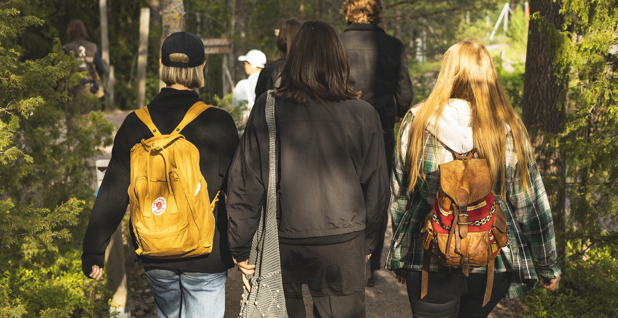 Ihmisiä kulkemassa metsässä, kuvattuna takaa